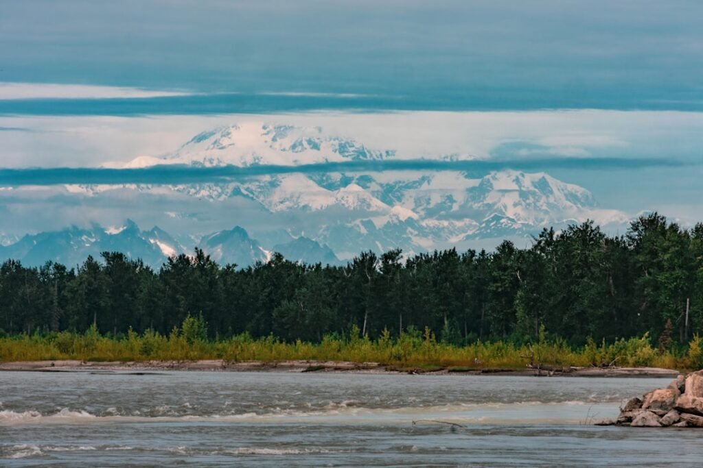 Mountain range rises above a river and trees.